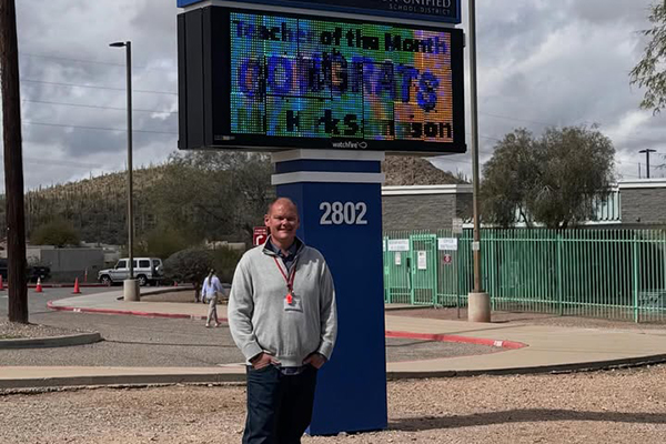 A man smiles in front of a school marquee