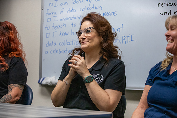 A woman sits with her hands folded, waiting to speak