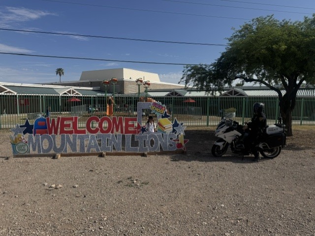 A motorcycle cop parks in front of the school next to a banner reading Welcome Mountain Lions
