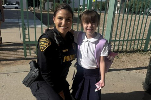 A female police officer smiles as she poses for a photo with a young girl
