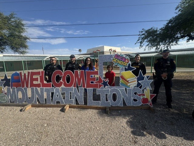 A student, staff and Tucson Police officers pose behind the Welcome Mountain Lions sign